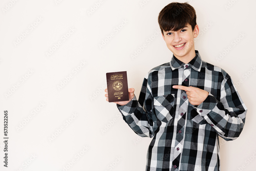 Young teenager boy holding Qatar passport looking positive and happy standing and smiling with a confident smile against white background.
