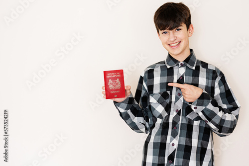 Photography Young teenager boy holding Singapore passport looking positive and happy standing and smiling with a confident smile against white background