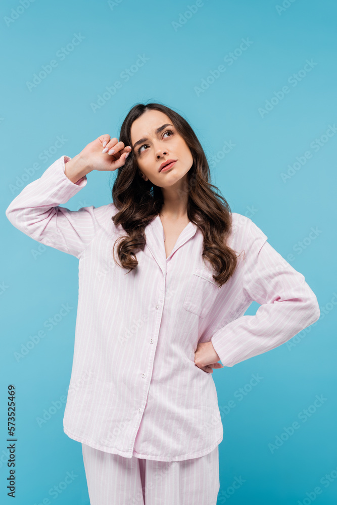 pensive young woman in sleepwear looking away and standing with hand on hip isolated on blue. pensive young woman in sleepwear looking away and standing with hand on hip isolated on blue.