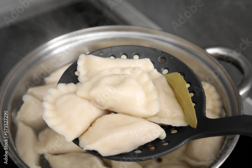 Dumplings (varenyky) with tasty filling on skimmer over pot indoors, closeup