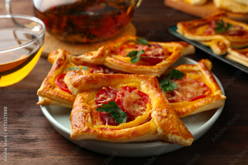 Fresh delicious puff pastry with cheese, tomatoes and parsley on wooden table, closeup
