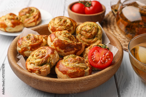 Fresh delicious puff pastry with tasty filling and tomato in bowl on white wooden table, closeup