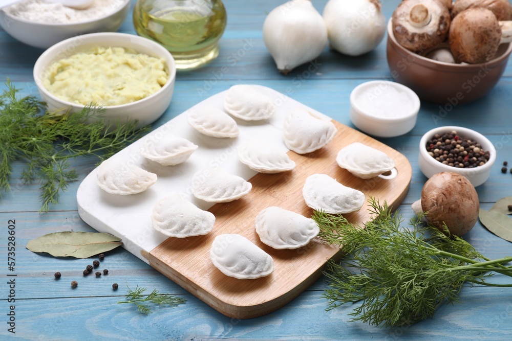 Raw dumplings (varenyky) and ingredients on light blue table