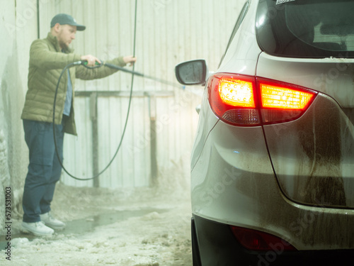 the guy washes a white SUV at a car wash in winter
