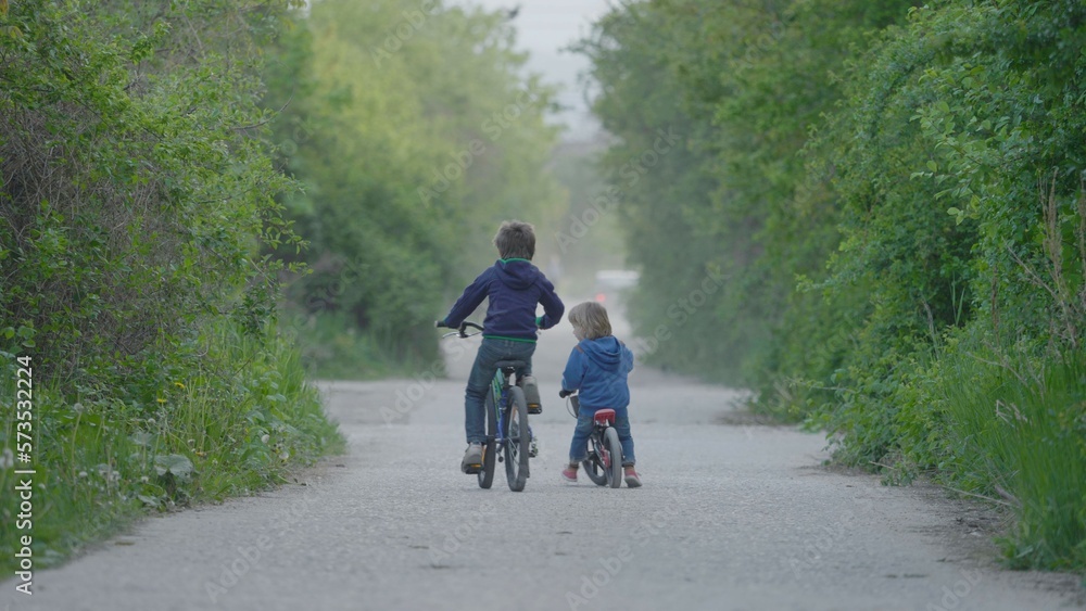 Two children riding bicycles on foggy and empty road, brother activities, nature