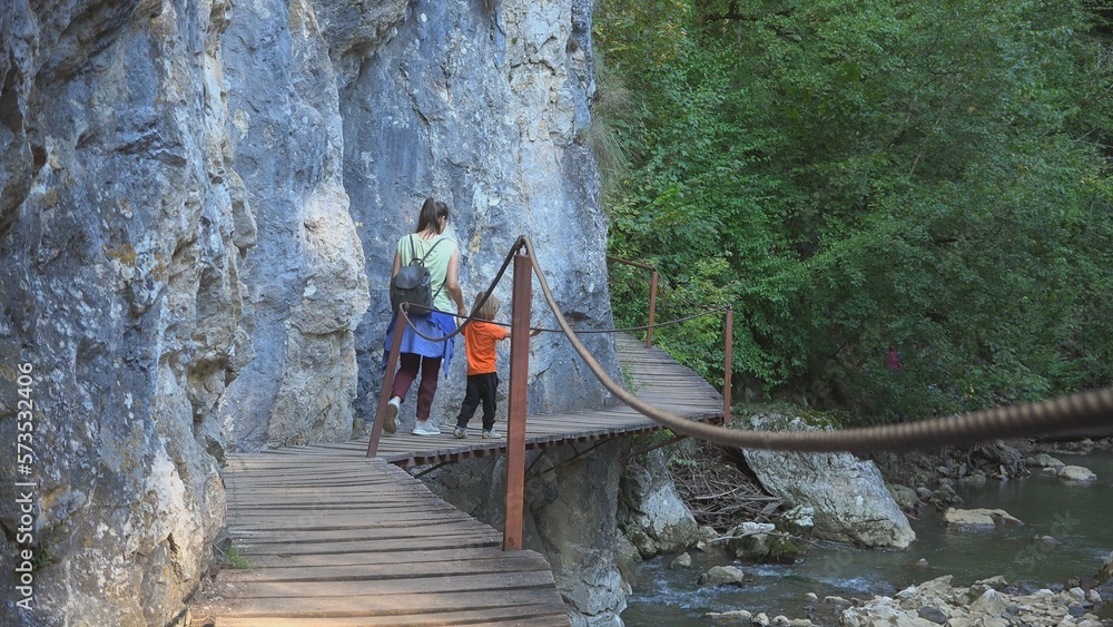 Mother and little child holding hand pass on footpath above mountain river Mother and little child holding hand pass on footpath above mountain river