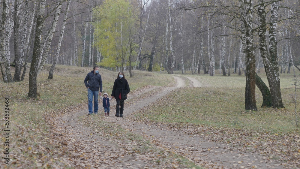 Parents with protective mask hand in hand with baby child walk in autumn forest Parents with protective mask hand in hand with baby child walk in autumn forest
