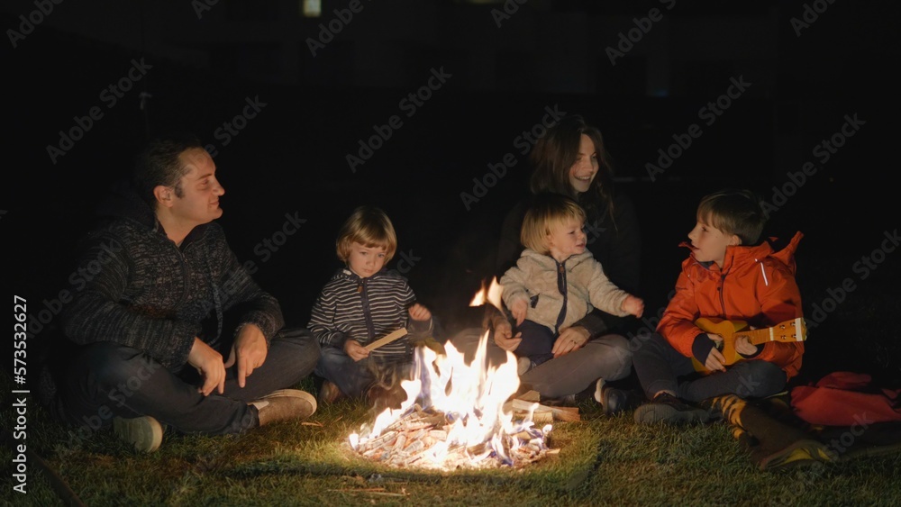 Mother, father and three children play at sing at campfire, emotional night