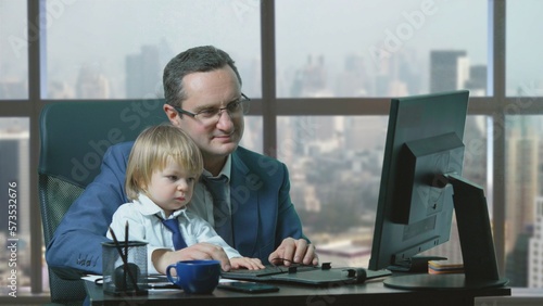 Father and little son with shirt and tie typing on computer, together work at office