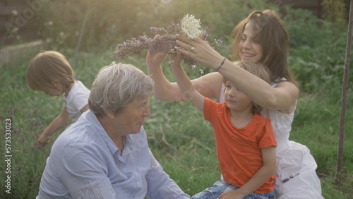 Young mother hold a child and arrange flower crown to old grandmother, happy