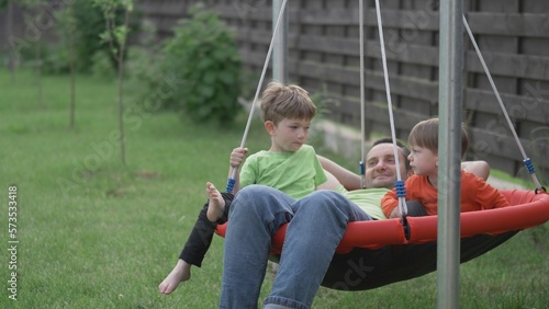 Little brothers enjoy the company of their father lying in a nest swing