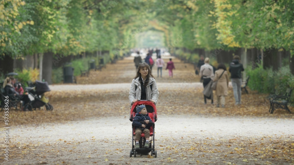 Single mother with kid in baby buggy walking on the alley in the park Single mother with kid in baby buggy walking on the alley in the park