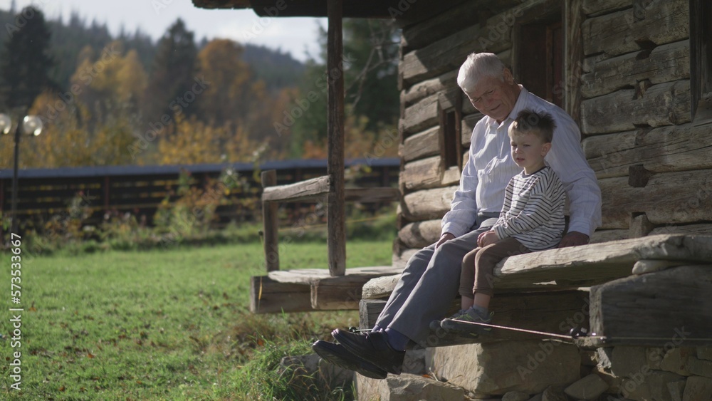 Elderly man with his grandson sit and talk on the wooden house porch