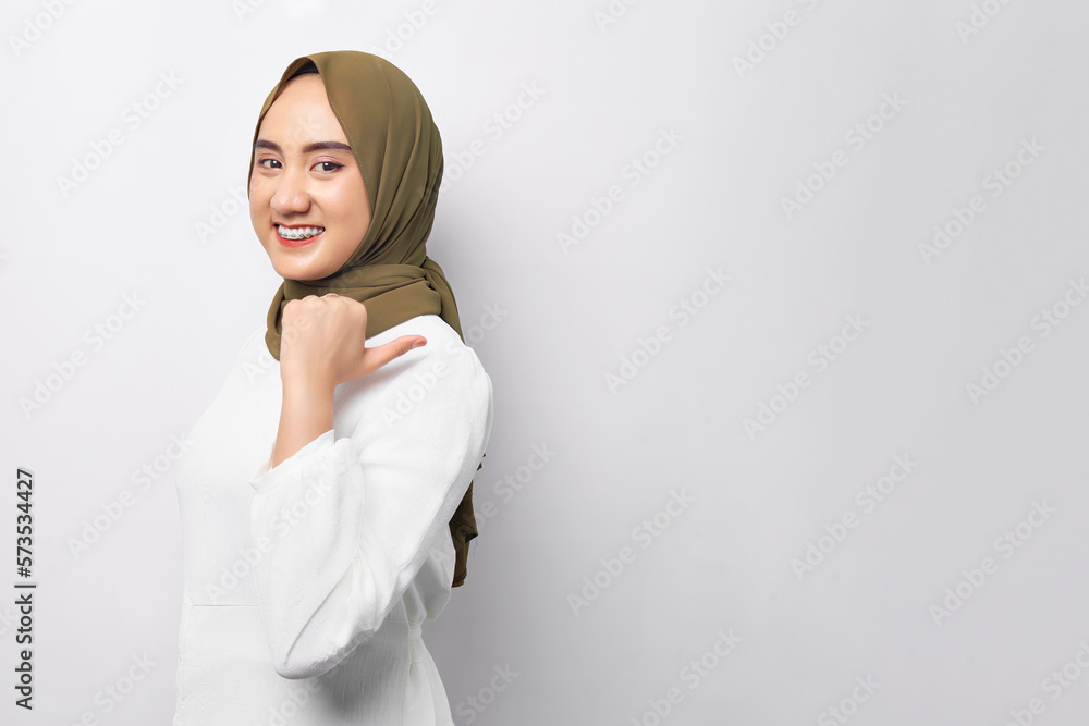 Beautiful smiling young Arabian Asian Muslim woman wearing hijab pointing thumb aside at blank space for text isolated on white background. People religious lifestyle concept Beautiful smiling young Arabian Asian Muslim woman wearing hijab pointing thumb aside at blank space for text isolated on white background. People religious lifestyle concept