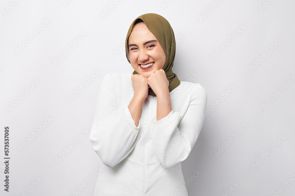 Smiling satisfied friendly young beautiful Asian Muslim woman 20s wearing hijab holding hand on her chin and looking at the camera isolated on white background. People religious lifestyle concept Smiling satisfied friendly young beautiful Asian Muslim woman 20s wearing hijab holding hand on her chin and looking at the camera isolated on white background. People religious lifestyle concept