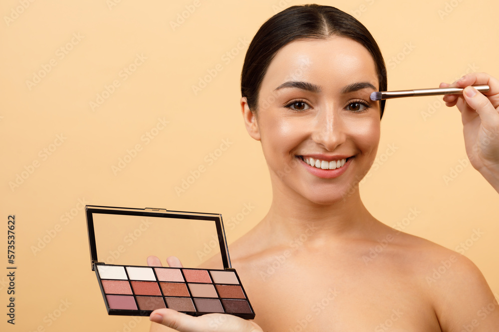 Hand Holding Eyeshadow Palette And Doing Makeup To Beautiful Young Indian Woman - obrazy, fototapety, plakaty 