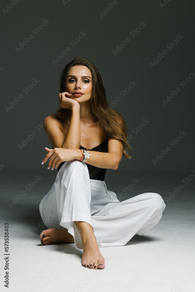 beautiful young woman in a trendy white suit sitting on the floor, a fashion portrait in the studio on a gray background beautiful young woman in a trendy white suit sitting on the floor, a fashion portrait in the studio on a gray background