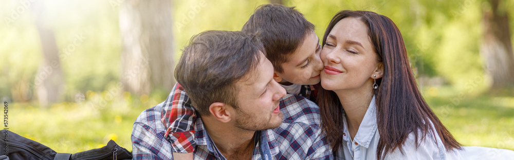 Happy family with kid lying on green grass in park. Mother and father hugging and kissing son. Happy family with kid lying on green grass in park. Mother and father hugging and kissing son.