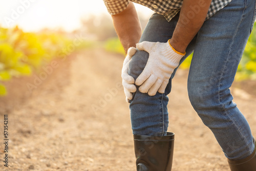 Injuries or Illnesses, that can happen to farmers while working. Man is using his hand to cover over knee because of hurt, pain or feeling ill.