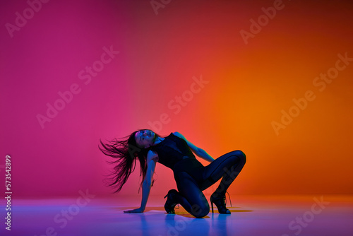 Passion in movements. Young woman performing high heel stiletto dance over gradient pink red studio background in neon light. Concept of contemporary dance style, art, aesthetics, hobby, creativity