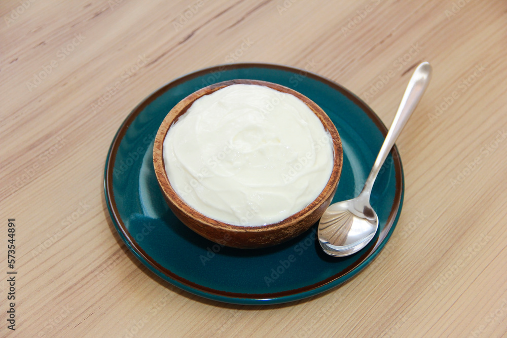 White fermented milk yogurt in a decorative brown plate on a wooden background White fermented milk yogurt in a decorative brown plate on a wooden background
