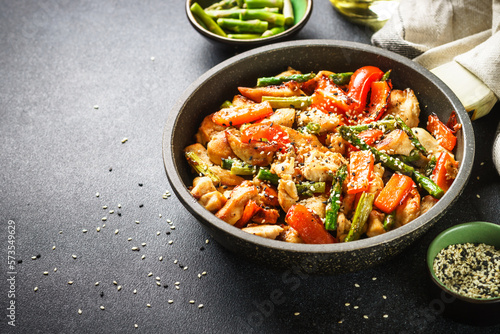 Chicken stir fry with vegetables and sesame in the skillet. Close up with copy space.