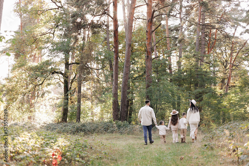 Back view of mother, father with three kids are walking, having fun in autumn forest. Family holding children hands enjoying time together at nature background. Happy parenthood and childhood concept