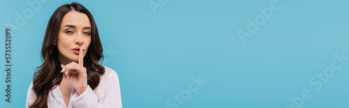 brunette young woman in sleepwear showing hush sign isolated on blue, banner.