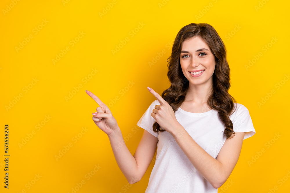 Closeup photo of gorgeous wavy brown hairstyle girl wear white t-shirt smiling directing fingers mockup promotion isolated on yellow color background Closeup photo of gorgeous wavy brown hairstyle girl wear white t-shirt smiling directing fingers mockup promotion isolated on yellow color background