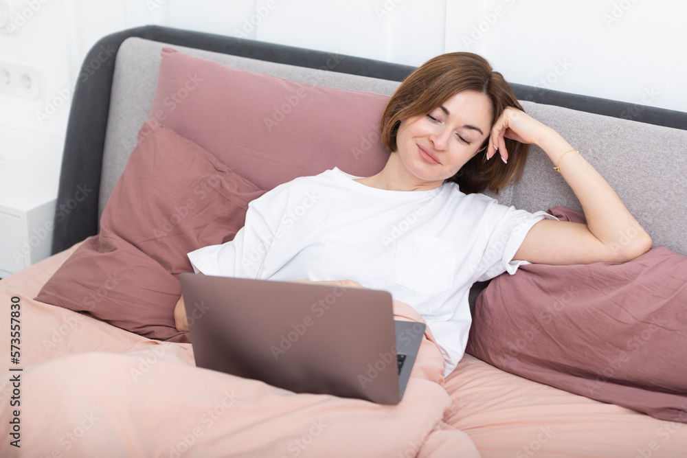 Attractive woman lying in the bed and working on laptop Attractive woman lying in the bed and working on laptop