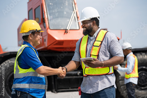 African American Engineer man shake hand with senior engineer and crane truck background at site work