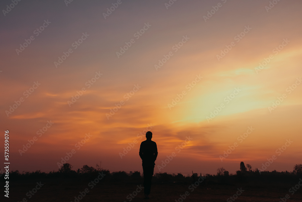 A person stands in silhouette against a sunset with orange and purple clouds. A person stands in silhouette against a sunset with orange and purple clouds.