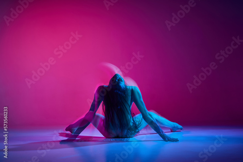 Passionate movements. Young woman dancing in bodysuit over gradient pink studio background in neon with mixed lights. Concept of contemporary dance style, art, aesthetics, hobby, creative lifestyle