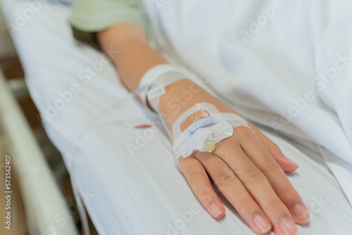 Young patient asian woman lying on bed in hospital with IV saline drip to back of the hand, teenager sick in hospital, Selective focus, healthcare and health insurance concept.