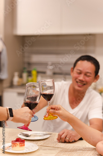 Asian man having a celebration with friends toasting glass of red at dinner party.