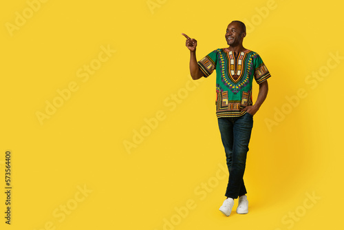 Cheerful black man in traditional shirt pointing at copy space