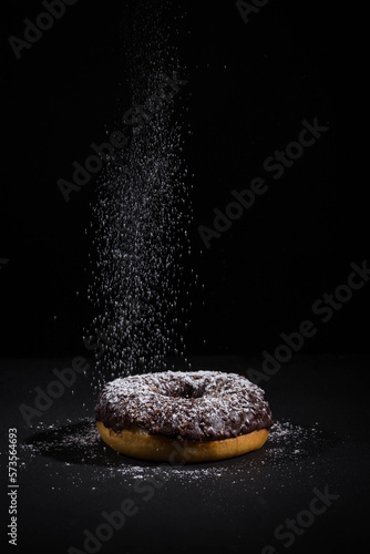 Sprinkling sugar powder on chocolate donut