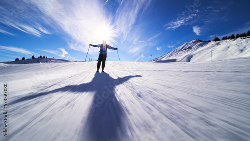 Silhouette of a skier skiing on slopes in the Swiss alps towards the camera. Hands widely spread out.