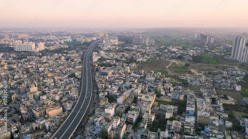 aerial drone shot flying forward over the elevanted sohna gurgaon road with vehicles passing over surrounded by densely packed houses shops and small businesses in Delhi NCR
