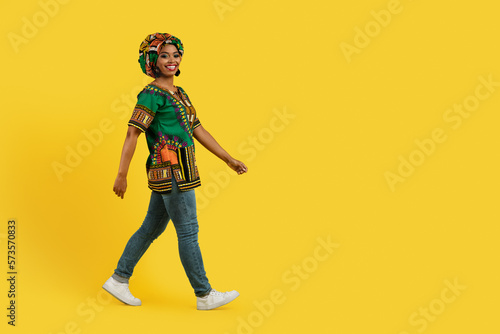 Cheerful black woman in traditional outwear walking towards copy space