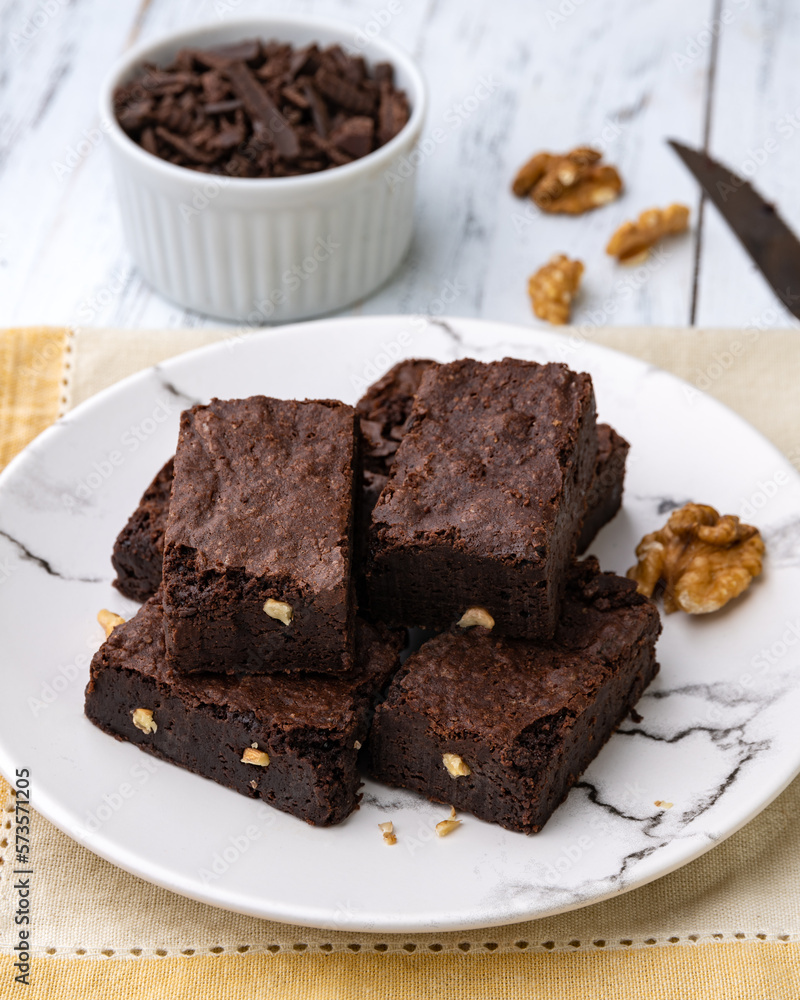 Brownies on a plate with chocolate pieces and syrup over white wooden table Brownies on a plate with chocolate pieces and syrup over white wooden table