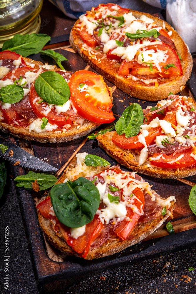 Hot loaded pizza sandwiches with tomatoes, mozzarella cheese and pepperoni, on dark background with herbs, olive oil and spices Hot loaded pizza sandwiches with tomatoes, mozzarella cheese and pepperoni, on dark background with herbs, olive oil and spices