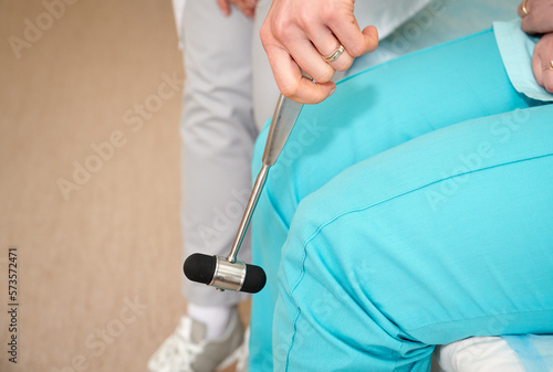Pretty female orthopedist with patient in her office. Young doctor neurologist examining her patient with hammer. Neurologist checks the reflexes of a middle age female patient. Close up view.