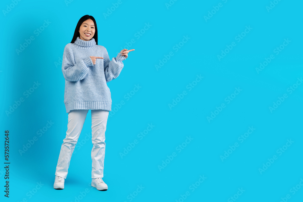 Cute asian woman in warm sweater pointing at copy space Cute asian woman in warm sweater pointing at copy space