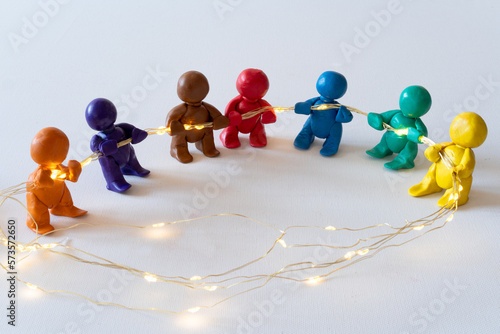Figuren aus Knete halten eine Lichterkette, symbolische Darstellung für Zusammenhalt. 