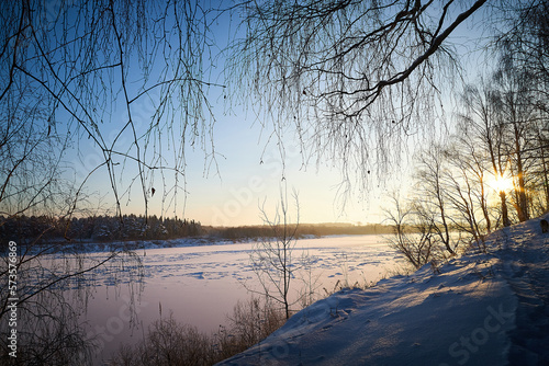 Sunrise on winter morning and trees with bare branches on a cold sunny time and snow on field. Partial focus