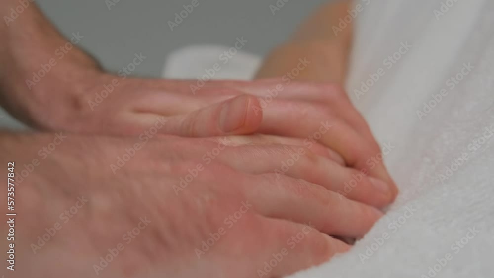 Hands of a manual therapist are massaging a woman's hand with white manicure. The camera is focused on the woman's fingers. Extreme closeup shot. Hands of a manual therapist are massaging a woman's hand with white manicure. The camera is focused on the woman's fingers. Extreme closeup shot.