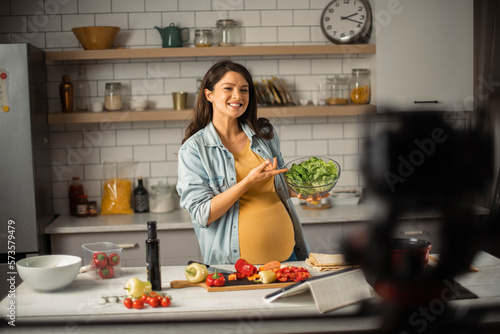 Beautiful pregnant woman filming cooking vlog. Happy woman filming her blog about healthy food at home.