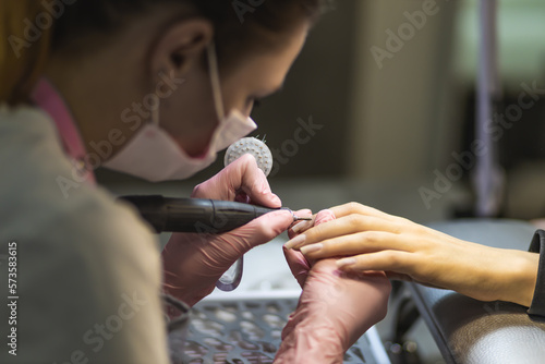 The manicurist cleans and removes the cuticle from the nail plate. Manicure process. Cut manicure technique. Special equipment for trimmed manicure.