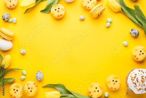 Fotografia Frame composition made of macaroon chicks, tulips, candy chocolate eggs, quail eggs and easter bread over yellow background